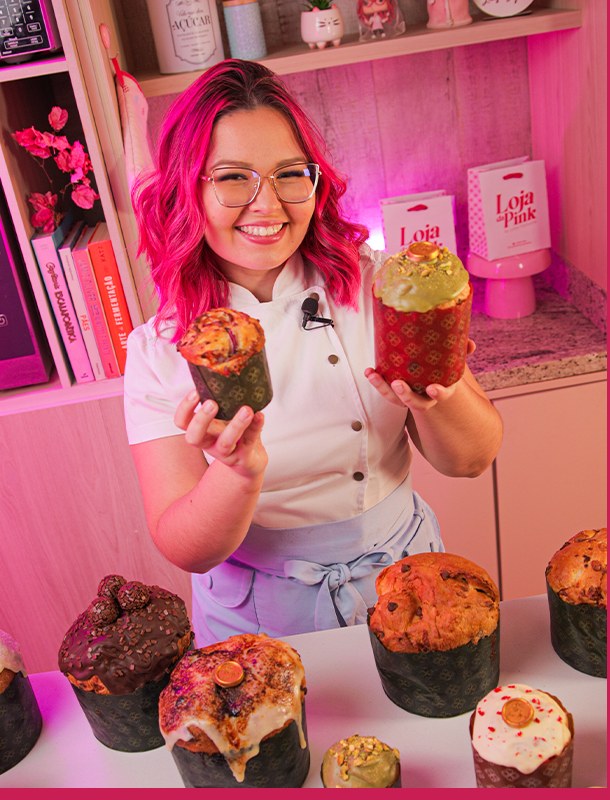 Chef Laíse Lopes segurando dois panetones decorados na cozinha rosa
